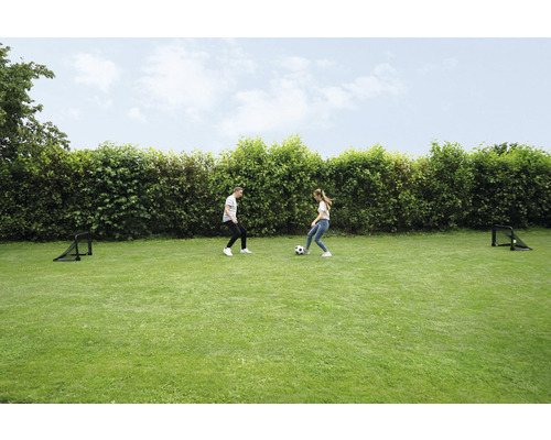 Dve osoby hrajú s futbalovou loptou na trávniku s dvoma futbalovými bránkami.