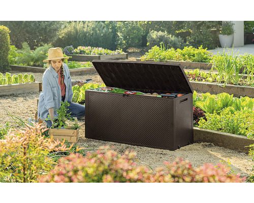 Záhradná scéna so ženou pracujúcou v blízkosti otvoreného hnedého záhradného boxu