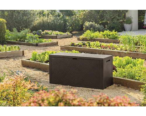 Záhradná scéna s hnedým záhradným boxom na štrku medzi zeleninovými záhonmi.