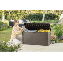 Žena ukladá deky a vankúše do hnedej záhradnej truhlice vonku.