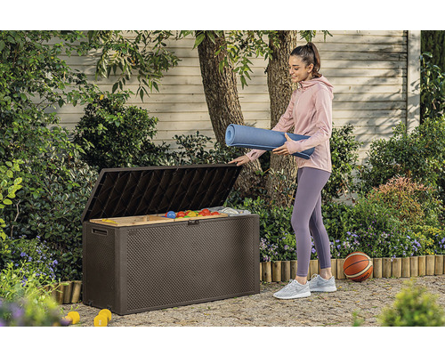 Žena ukladá podložku na jogu do hnedej záhradnej bedne vonku.