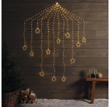 Dekoratívna svetelná reťaz s hviezdami pred drevenou stenou, so stromom, polenami a pohármi na sekt