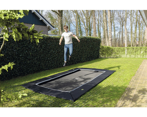 Záhradná trampolína v úrovni terénu so skákajúcim mužom v záhrade