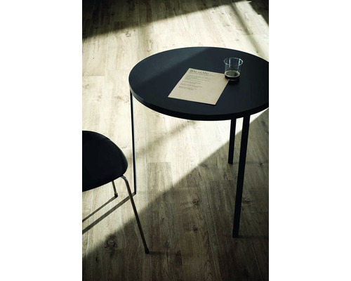 Scéna s okrúhlym stolom, stoličkou, nápojom a listom papiera na drevenej podlahe.