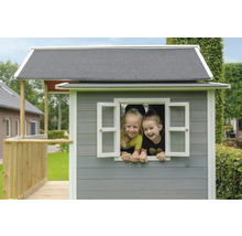 Dve deti sa pozerajú z okna sivého dreveného domčeka na hranie so sivou strechou