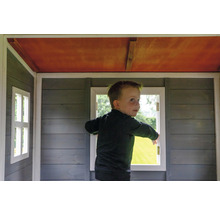 Dieťa stojí v drevenom hracom domčeku s oknami