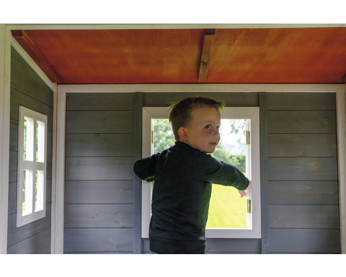 Dieťa stojí v drevenom hracom domčeku s oknami