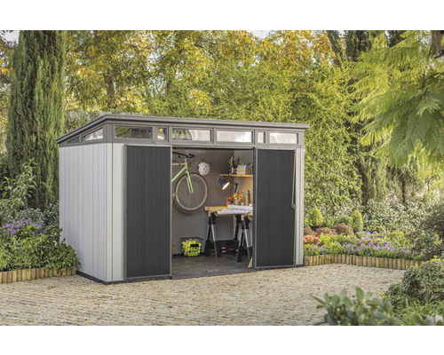 Záhradný domček s otvorenými dverami, umiestnený v záhrade a vybavený bicyklom a pracovným stolom