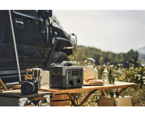 Scéna s prenosnou elektrárňou Ecoflow, kávovarom, fotoaparátom, dronom a kanvicou na drevenom stole vonku