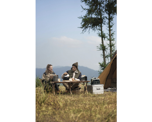 Dve osoby kempujú so stolom, stoličkami, kuchynským náčiním a stanom v prírode