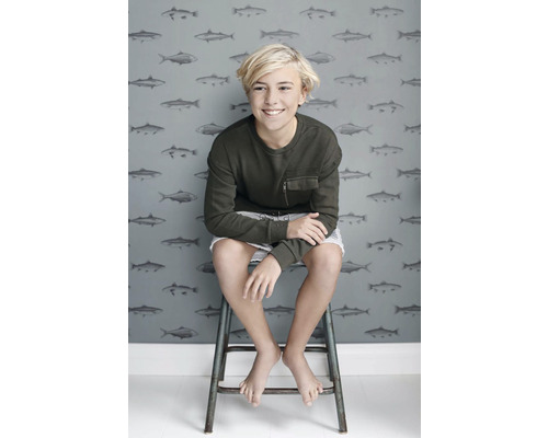 Dospievajúci sedí pred tapetou so vzorom rýb.