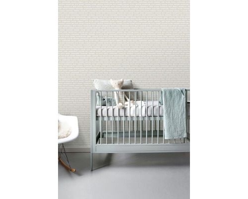 Svetlá detská izba s tapetou s nápismi, detskou postieľkou a hojdacím kreslom.