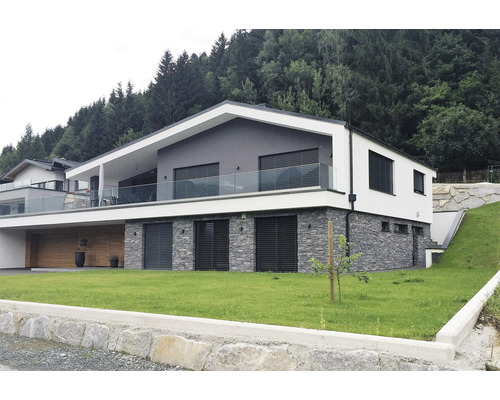 Moderný dom s kamennou fasádou a skleneným balkónom na svahu