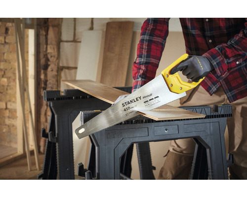 Osoba reže drevenú dosku ručnou pílou na pracovnom stole.