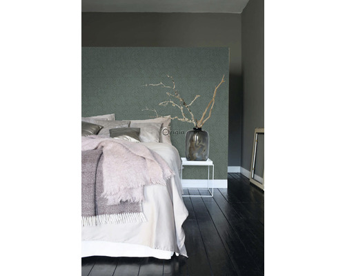 Spálňa s posteľou, nočným stolíkom, vázou s konármi a vzorovanou tapetou.