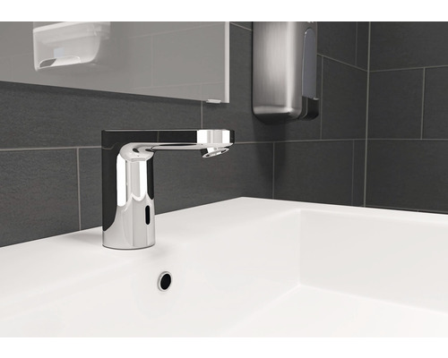 Bezkontaktná umývadlová batéria na bielom umývadle s tmavými obkladmi v pozadí