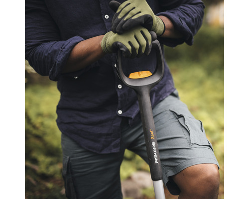 Osoba v záhradných rukaviciach drží rýľ značky Fiskars.