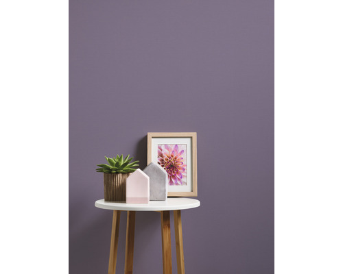 Dekoratívna scéna s hrnkovou rastlinou, domácimi dekoráciami a zarámovaným obrazom na malom stole pred stenou