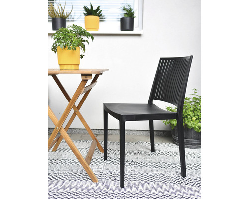 Scéna s čiernou plastovou záhradnou stoličkou, dreveným stolom a dekoráciou vonku.