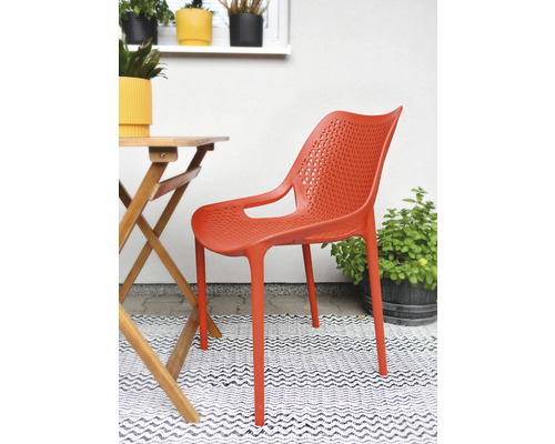 Oranžová plastová stolička s podrúčkami vedľa dreveného stola na terase