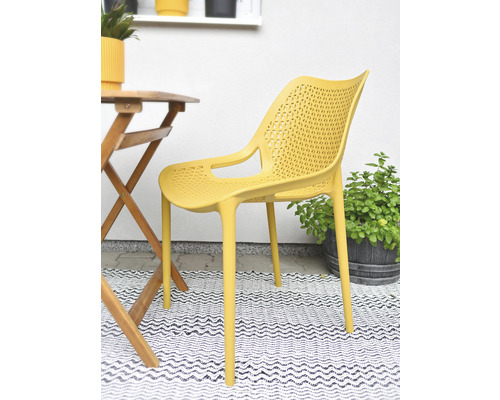 Žltá plastová stolička s podrúčkami vedľa dreveného stola na balkóne