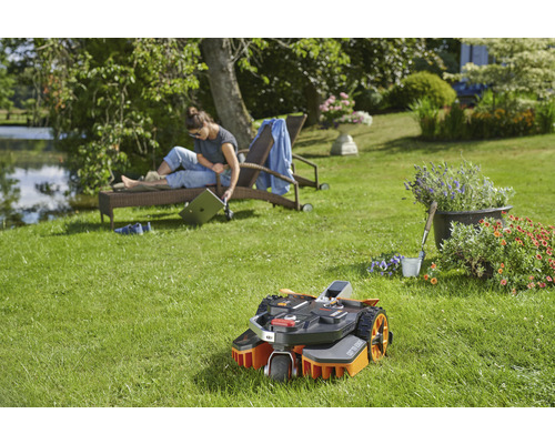 Scéna s robotickou kosačkou v záhrade, žena odpočíva na lehátku