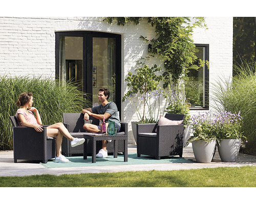 Záhradná scéna so sedacou súpravou, stolom a ľuďmi na terase pred domom.