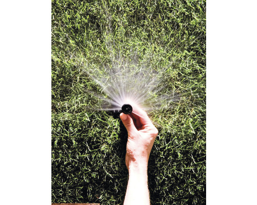 Ruka drží zavlažovač trávnika, ktorý strieka vodu.