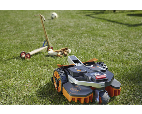 Robotická kosačka na trávniku s hračkami v pozadí