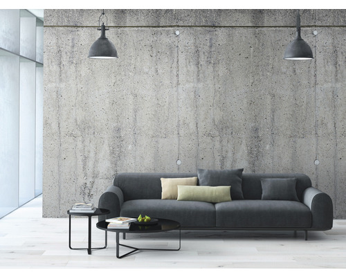 Obývacia izba so sivou pohovkou, konferenčným stolíkom a závesnými svetlami pred betónovou stenou.