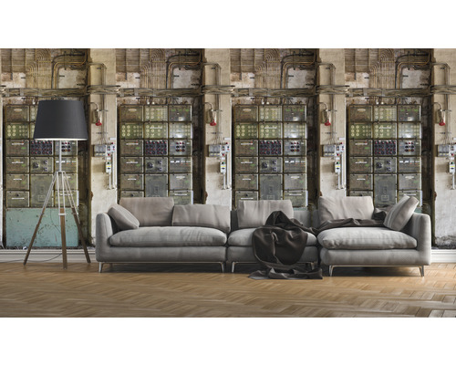 Obývacia izba so sivou pohovkou, stojacou lampou a nástennou tapetou s motívom rozvádzača pre industriálnu atmosféru.