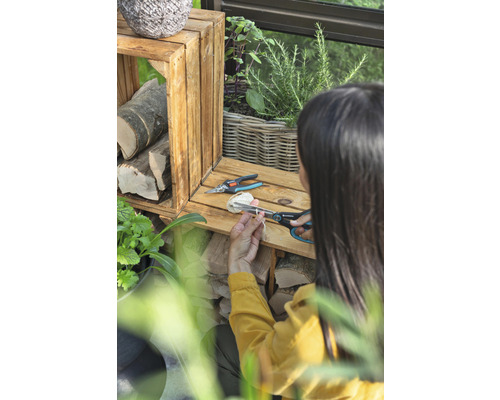 Žena strihá špagát záhradnými nožnicami vedľa drevených debničiek a rastlín.