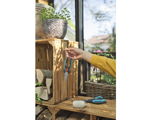 Scéna zo záhrady s kvetináčom, polenami, záhradnými nožnicami a osobou