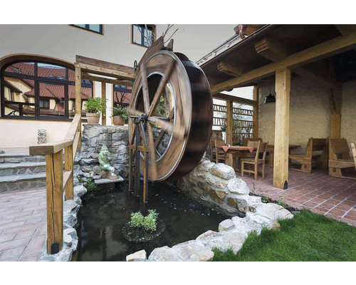Scéna s vodným kolesom, ktoré sa otáča v rybníku, obklopené kameňmi a zeleňou