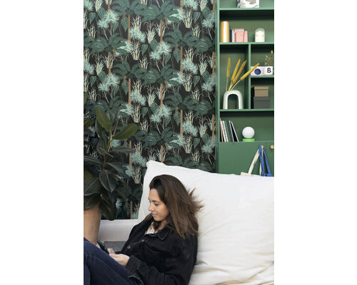 Obývacia izba s tapetou s motívom džungle, zelenými policami a ženou sediacou na sedacom vaku