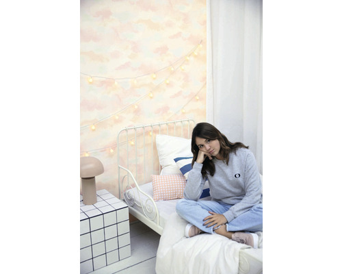 Svetlá spálňa s kovovou posteľou, svetelnou reťazou a mladou ženou