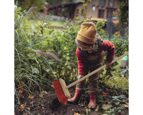 Dieťa zametá lístie v záhrade s pouličnou metlou.