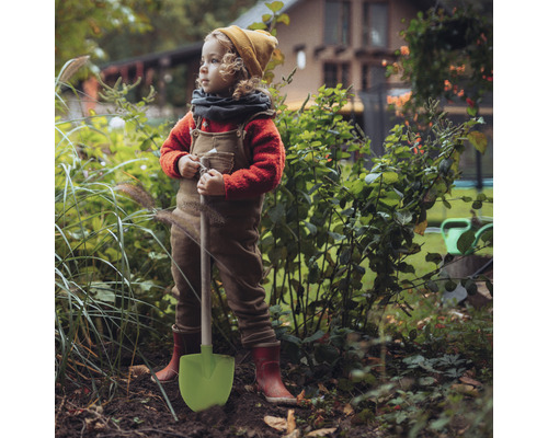 Dieťa s lopatou stojí v záhrade.