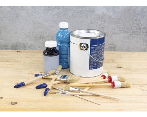 Vedro s farbou, fľaša s lakom a štetce na drevenom stole
