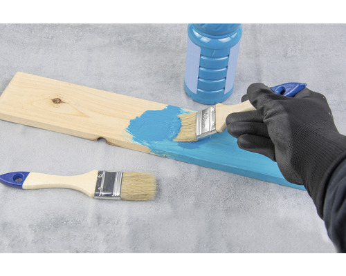 Osoba natiera drevenú dosku štetcom a farbou.