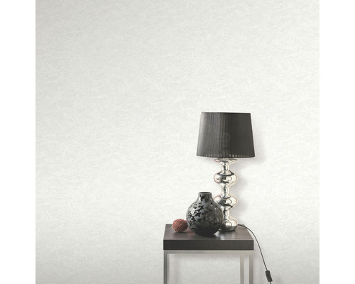 Svetlá tapeta s textúrou, stolná lampa, dekorácia a stolík v izbe.