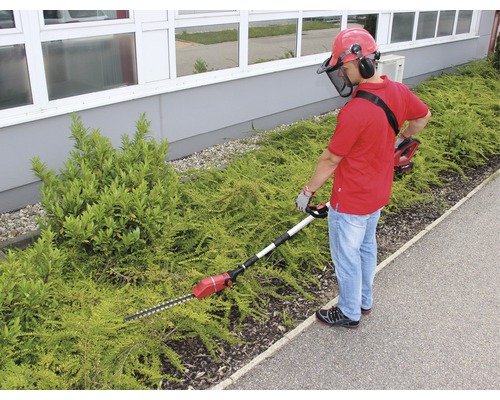 Muž strihá živý plot akumulátorovými nožnicami na živý plot s teleskopickou tyčou a ochranným zariadením
