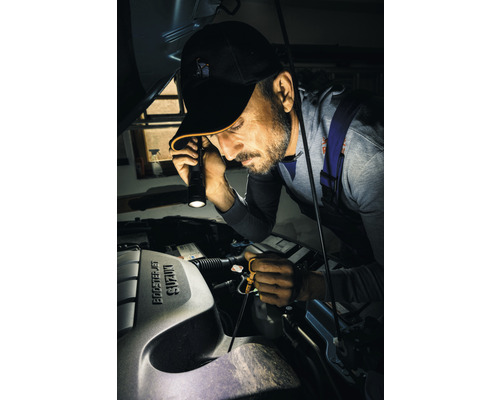 Muž kontroluje motorový priestor auta s baterkou.