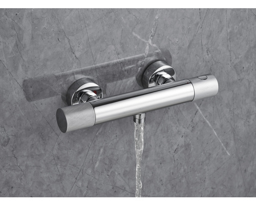 Termostatická batéria na omietku s prúdom vody pred sivou stenou