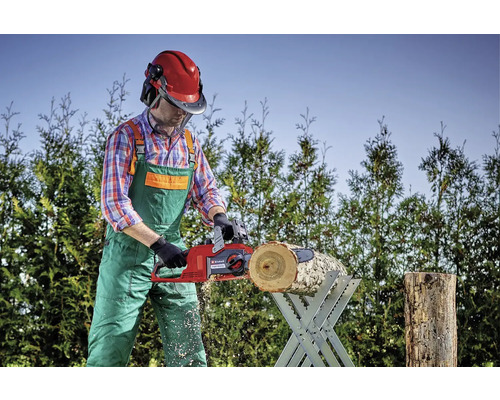 Osoba reže kus dreva na kozli na rezanie dreva pomocou elektrickej reťazovej píly.