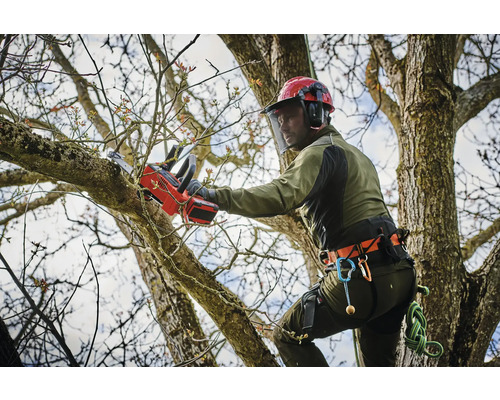 Arborista s helmou a ochranným odevom na rezanie konárov s akumulátorovou pílou.