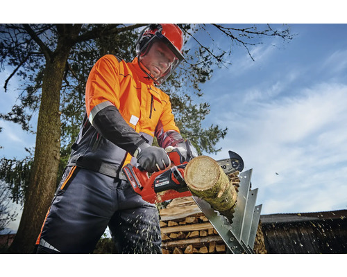 Osoba v ochrannom odeve píli akumulátorovou motorovou pílou kus dreva na kozlíku.