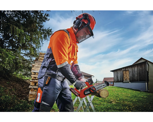 Osoba s ochrannou prilbou a chráničmi sluchu pracuje vonku s akumulátorovou pílou.