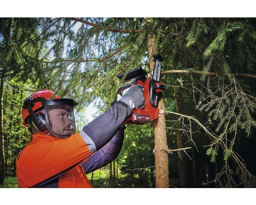 Osoba s bezpečnostným vybavením používa akumulátorovú pílu na rezanie konára stromu.