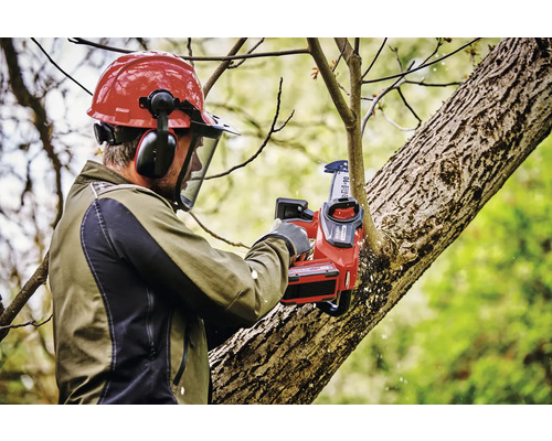 Muž s ochrannou prilbou a akumulátorovou pílou prerezáva konáre stromov
